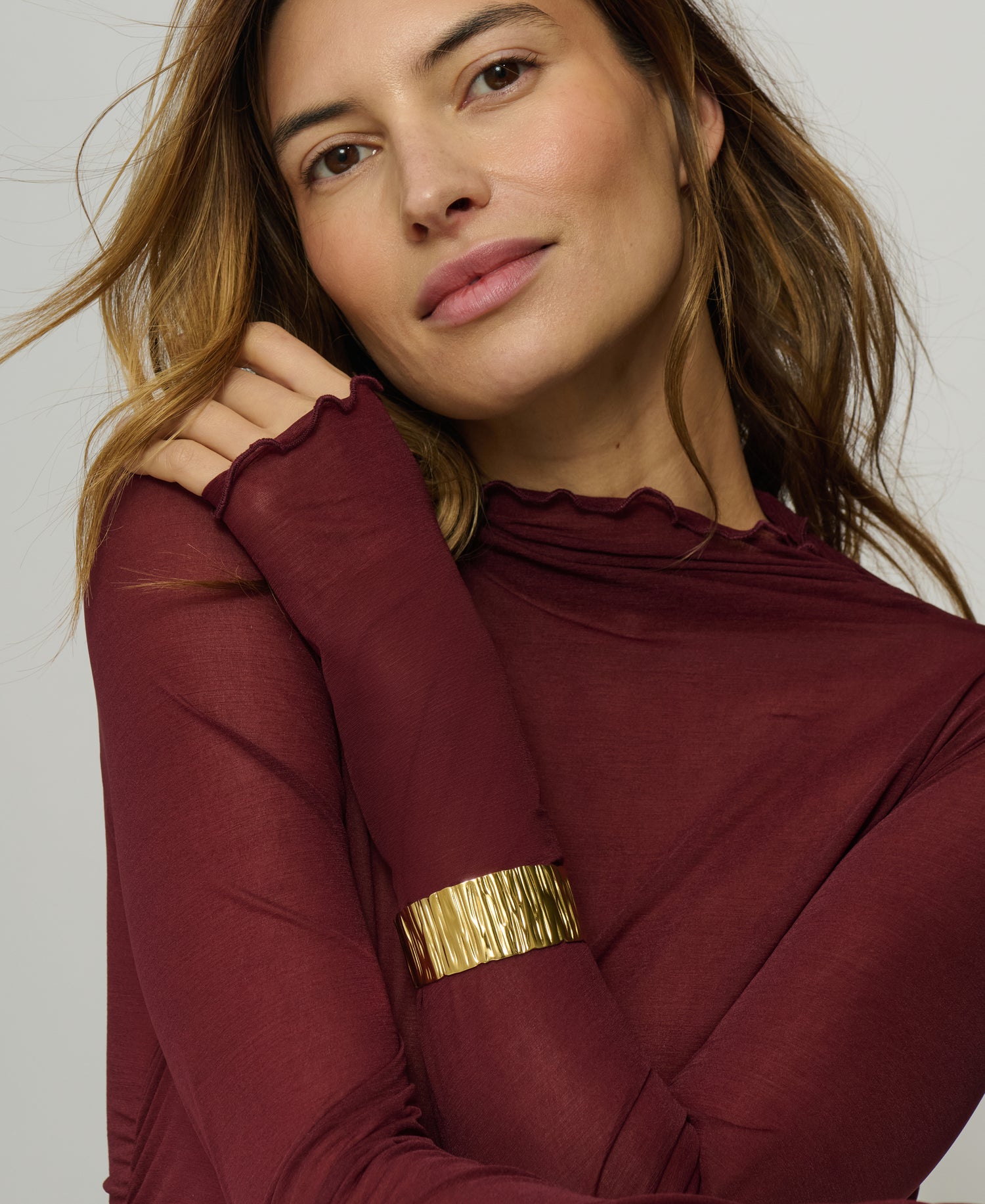 Woman wearing a burgundy top with a gold band on a white background