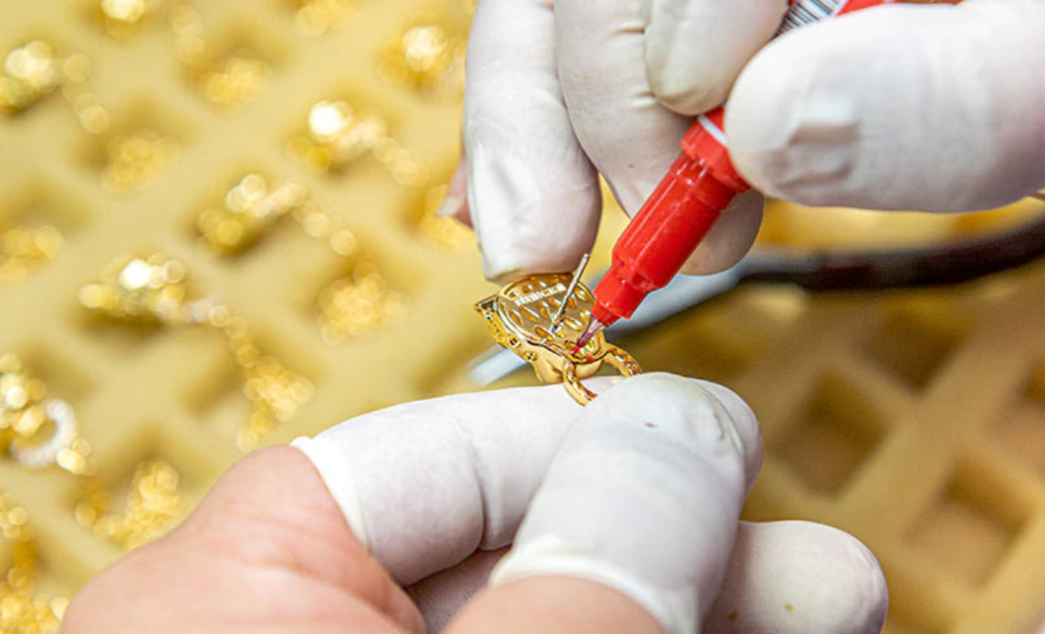 Gold jewelry being worked on with a red tool against a gold background