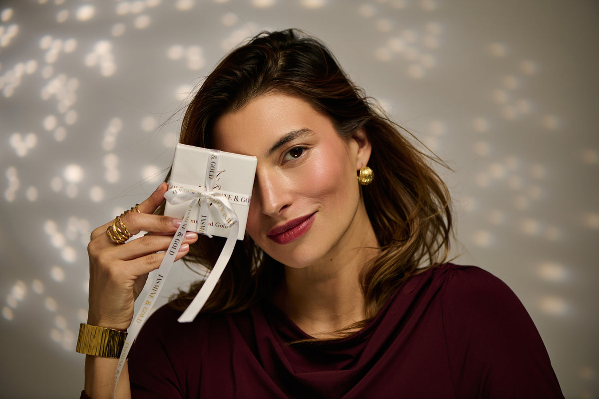 Woman wearing gold chunky cuff and gold chunky earrings holding a present on a Christmassy background 