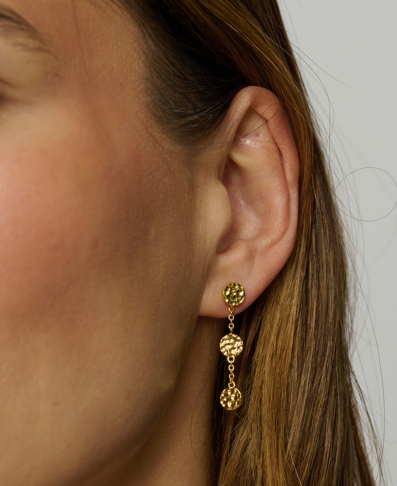 Close-up of a person wearing gold earrings with a plain background