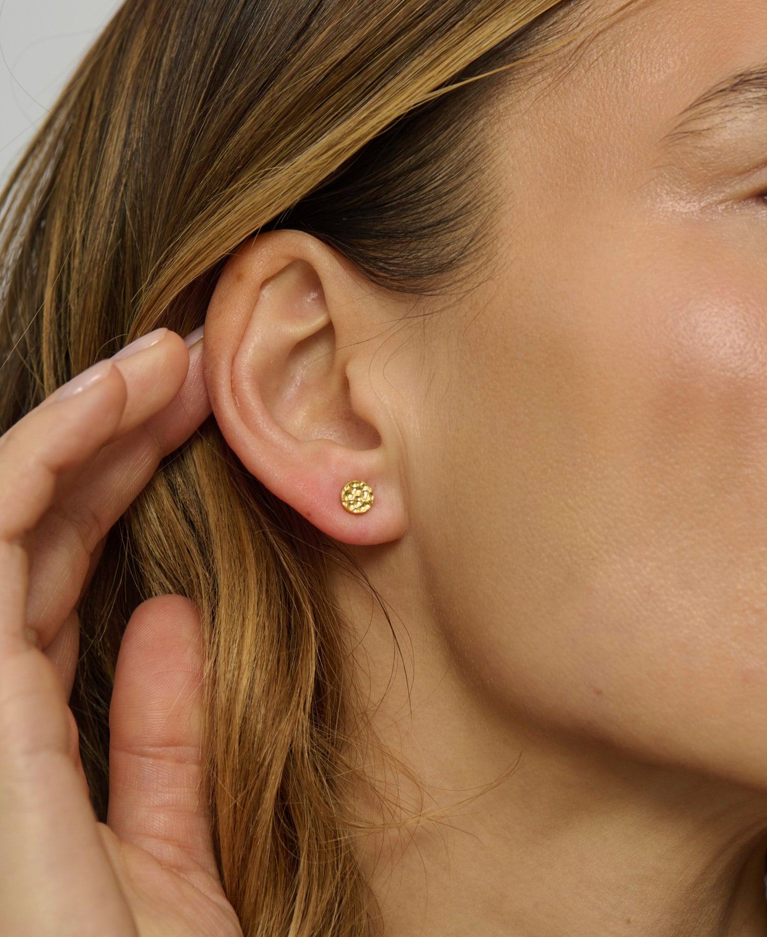 Close-up of a person wearing gold earrings with a blurred background
