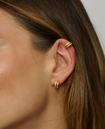 Close-up of a person wearing gold hoop earrings with a neutral background