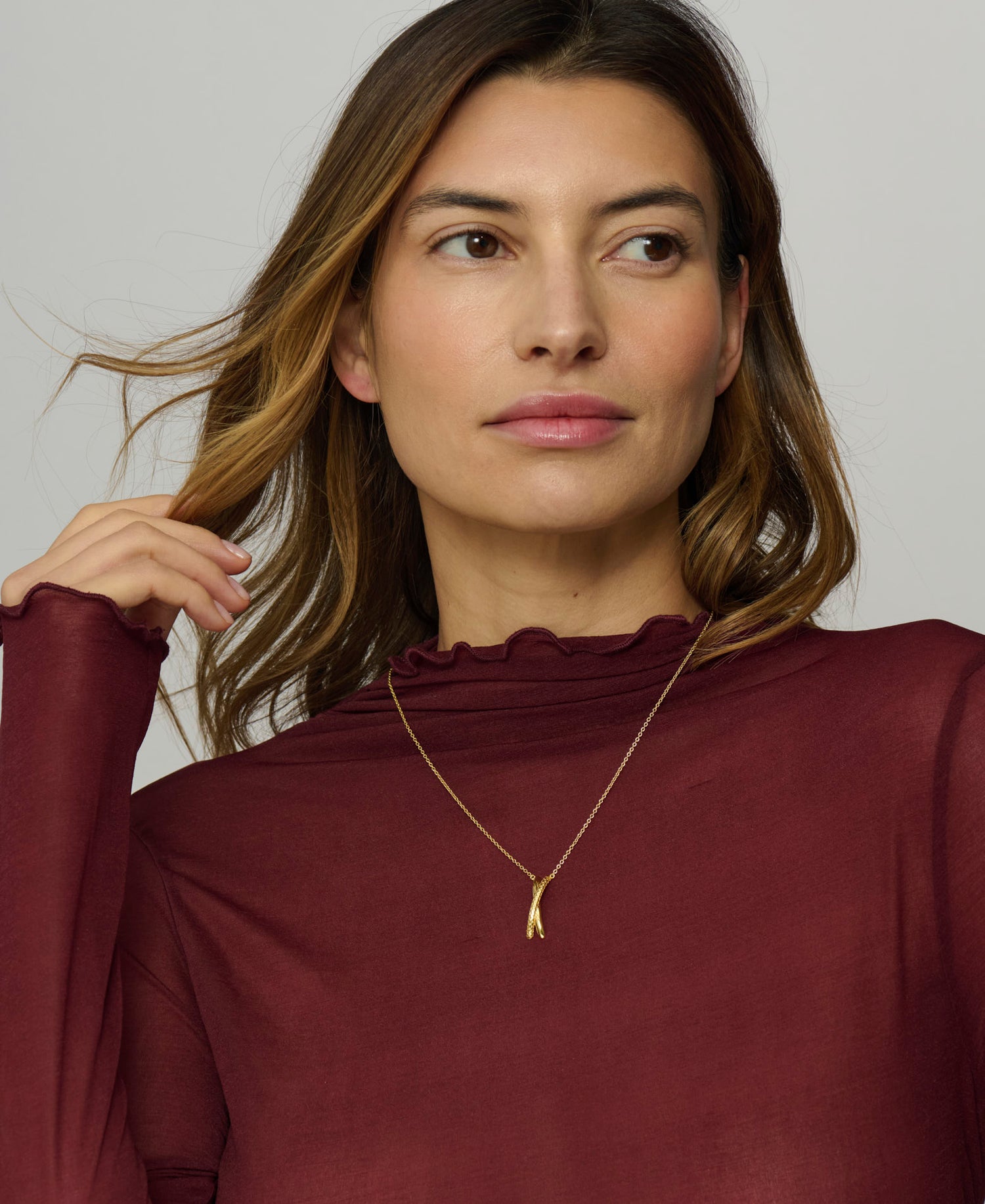 Woman wearing a burgundy top and gold necklace against a neutral background