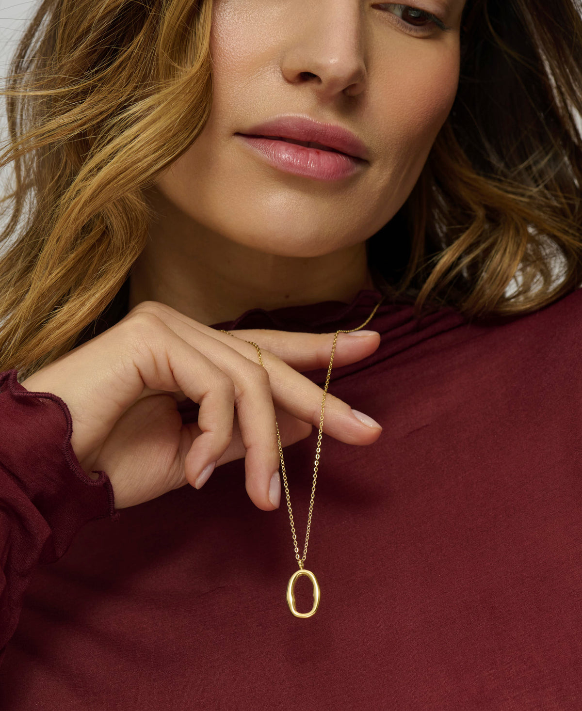 Woman wearing a gold necklace with an oval pendant, close-up of face and hand.