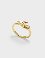 Gold ring with a pearl and leaf design on a light gray background