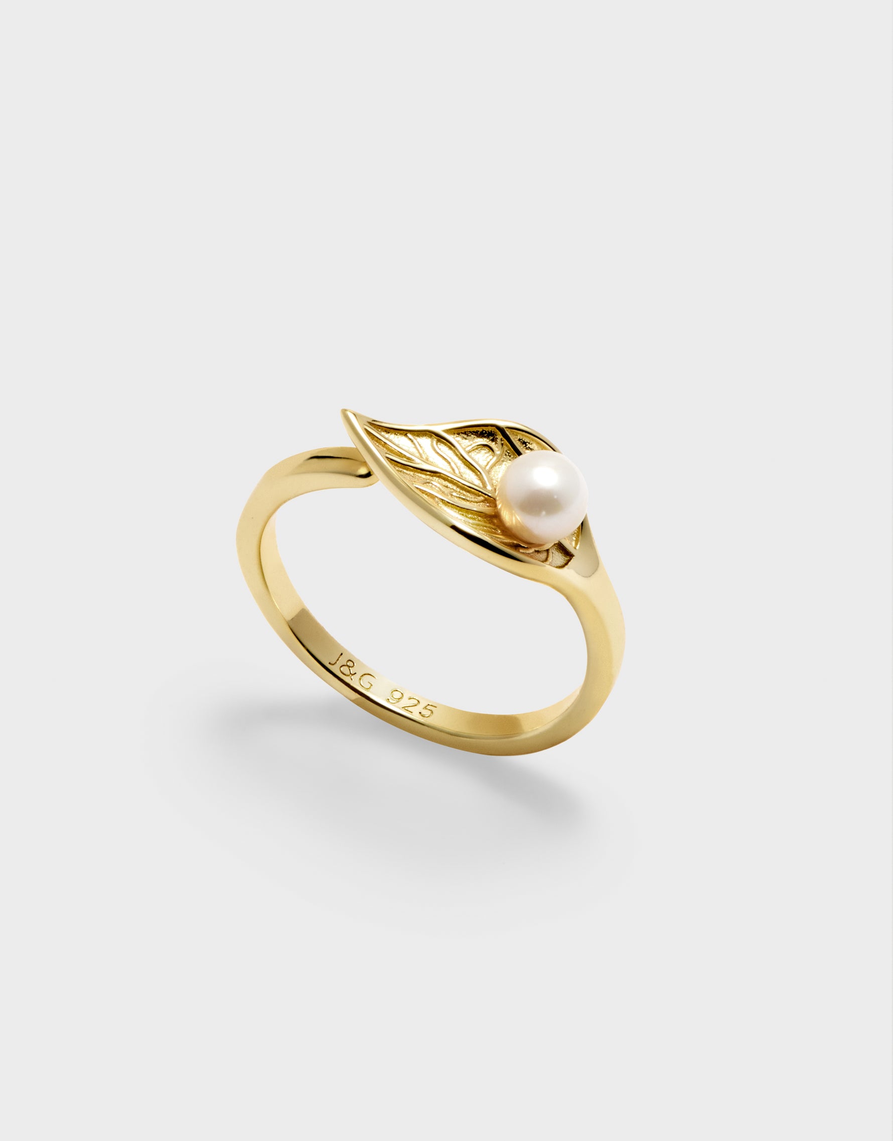 Gold ring with a pearl and leaf design on a light gray background