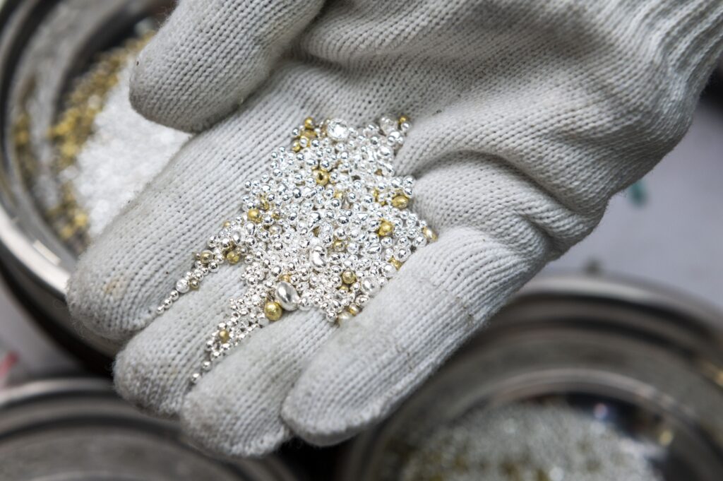 Hand wearing a  glove holding small pieces of recyclable silver and gold.