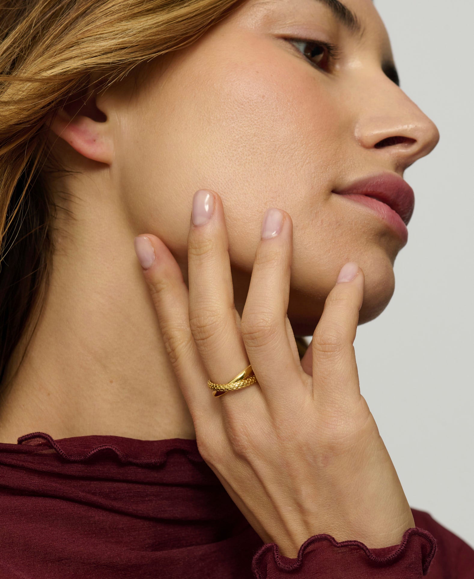 Woman wearing a gold ring on her finger, touching her face with her hand.