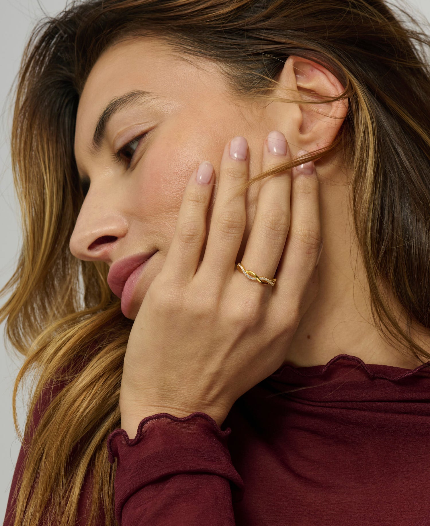 Woman with hand near ear, wearing a gold ring, against a neutral background