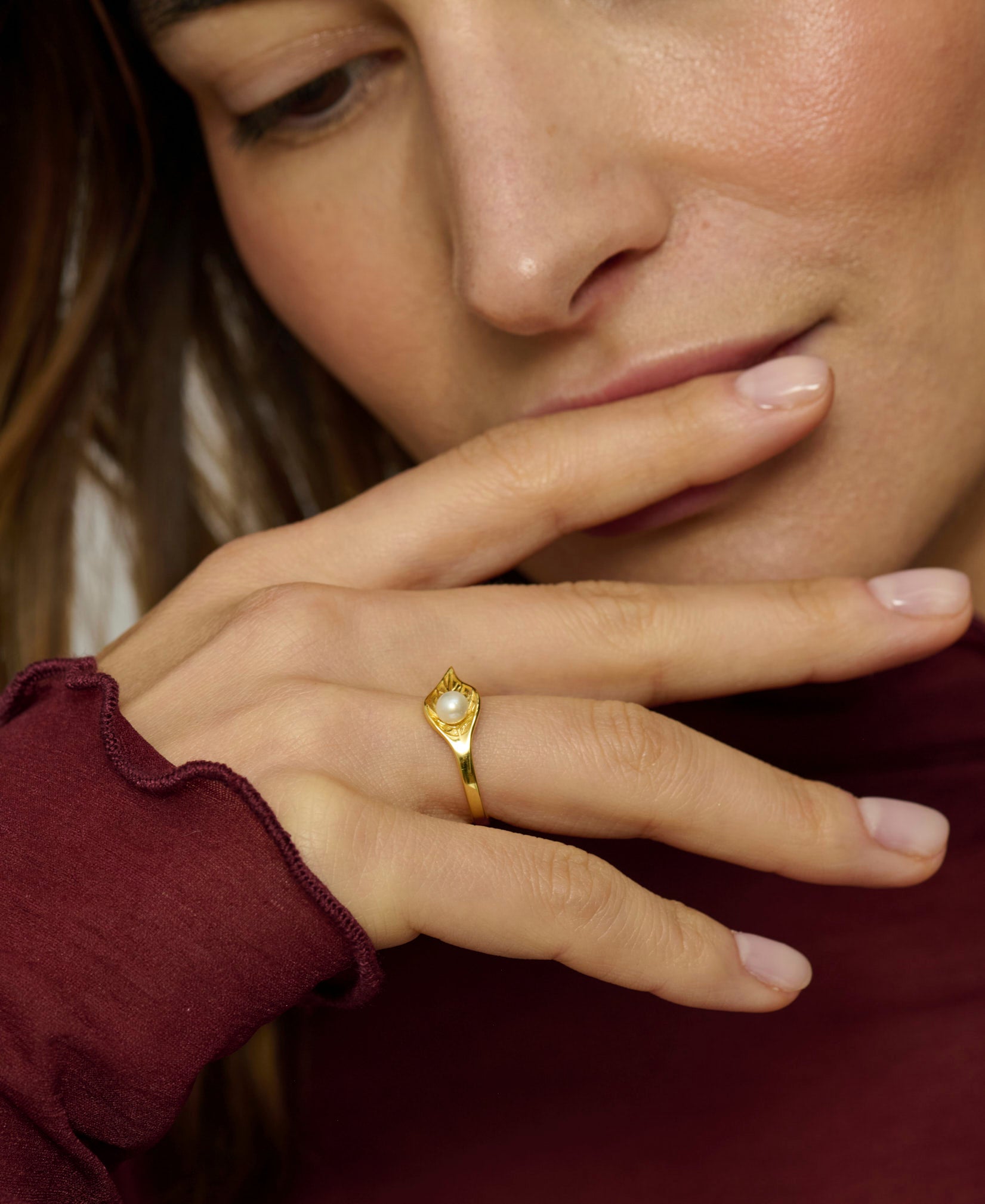Close-up of a woman's hand wearing a gold ring with a diamond, touching her face.