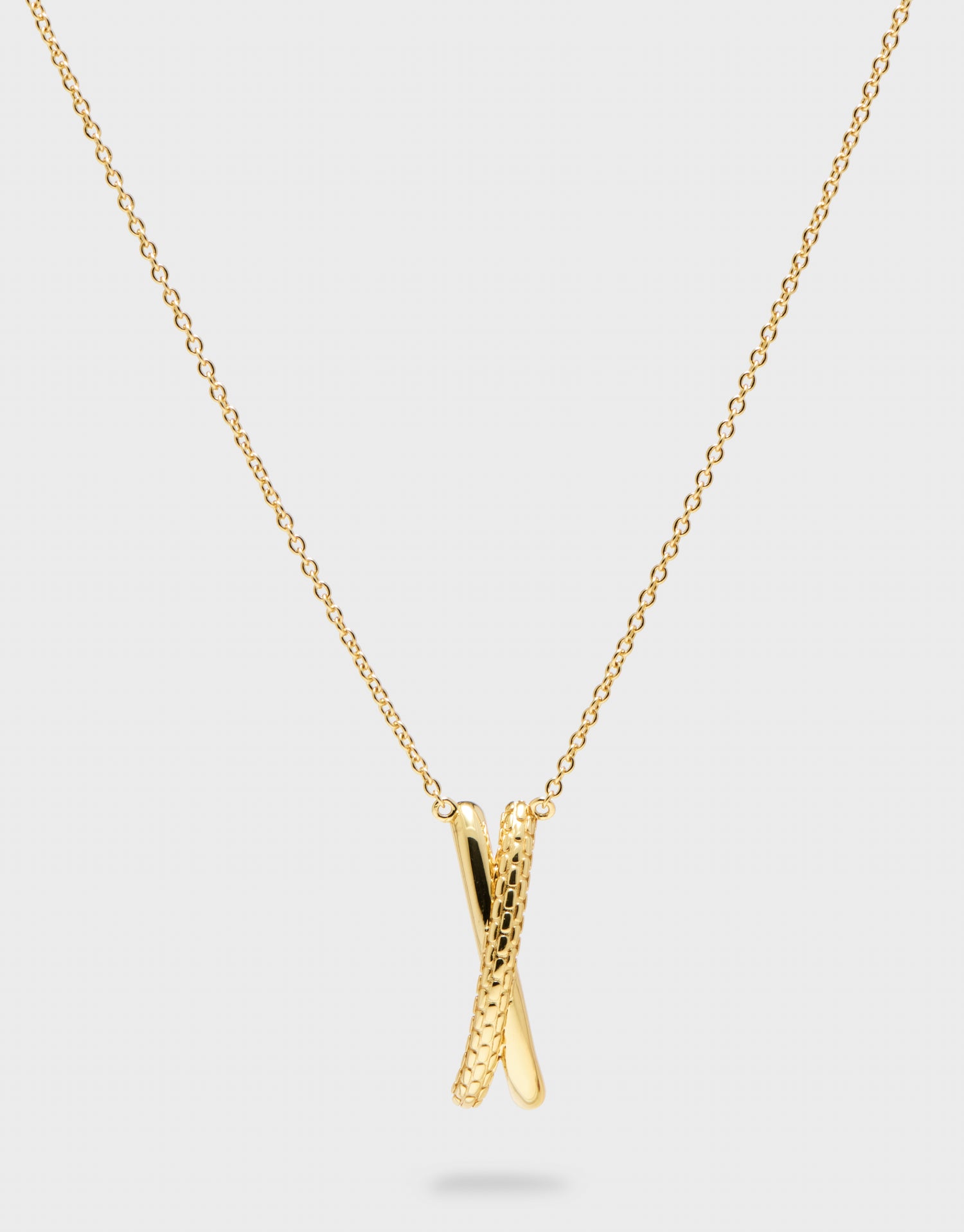 gold pendant X necklace with gold chain on grey background 