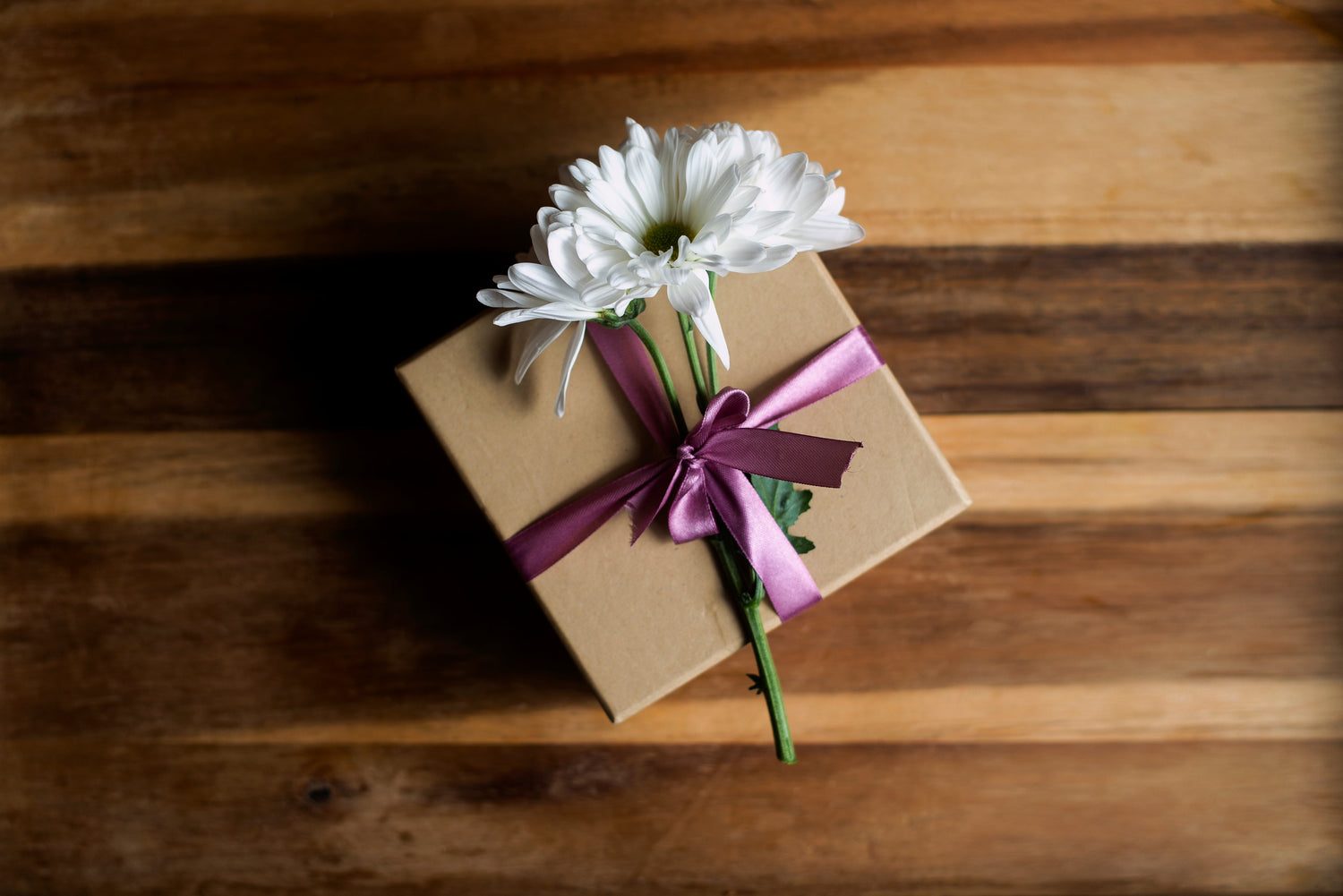 Gift box with white flowers and a purple ribbon on a wooden surface